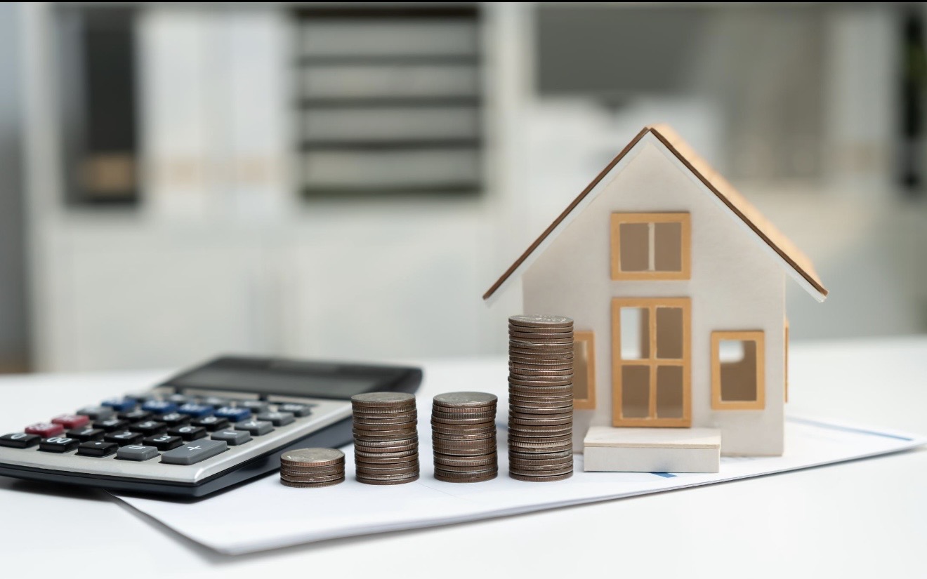 A miniature house, calculator and stacks of coins illustrating property price and value